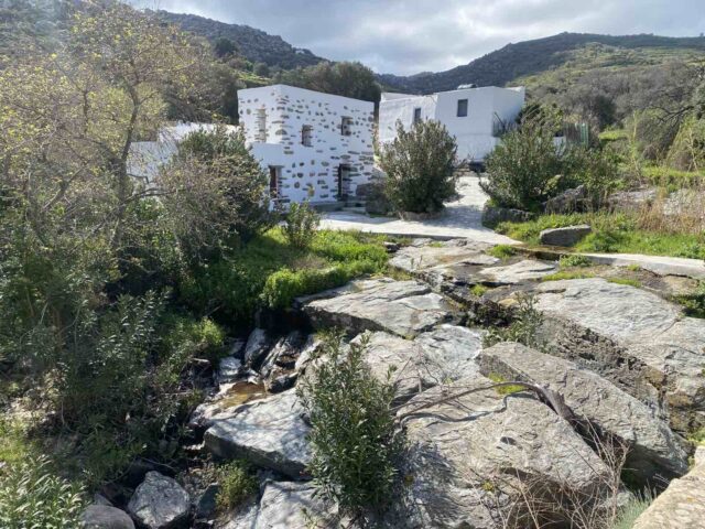 Παραδοσιακά πέτρινα και λευκά σπίτια του οικισμού Αγάπη στην Τήνο, δίπλα σε ρυάκι.