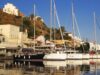 Ιστιοφόρα και σκάφη αγκυροβολημένα στο λιμάνι του Κόρφου στην Κέα, με παραδοσιακά κτίρια στο φόντο.
