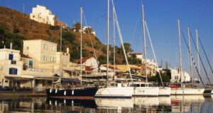 Ιστιοφόρα και σκάφη αγκυροβολημένα στο λιμάνι του Κόρφου στην Κέα, με παραδοσιακά κτίρια στο φόντο.